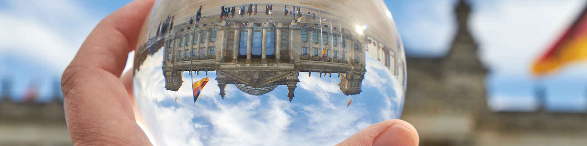 Hand mit Glaskugel, die den Berliner Reichstag auf dem Kopf stehend zeigt