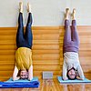 Foto: zwei Frauen üben Yoga-Kopfstand an der Wand