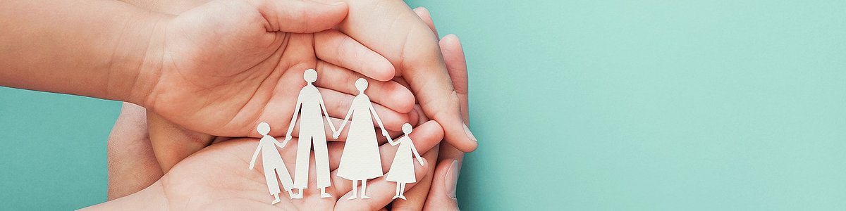 Hände von Erwachsenen und Kindern zeigen Scherenschnitt einer Familie