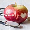 Foto: roter Apfel, in den ein Herz und eine Herzlinie eingeritzt ist, sowie ein Stethoskop