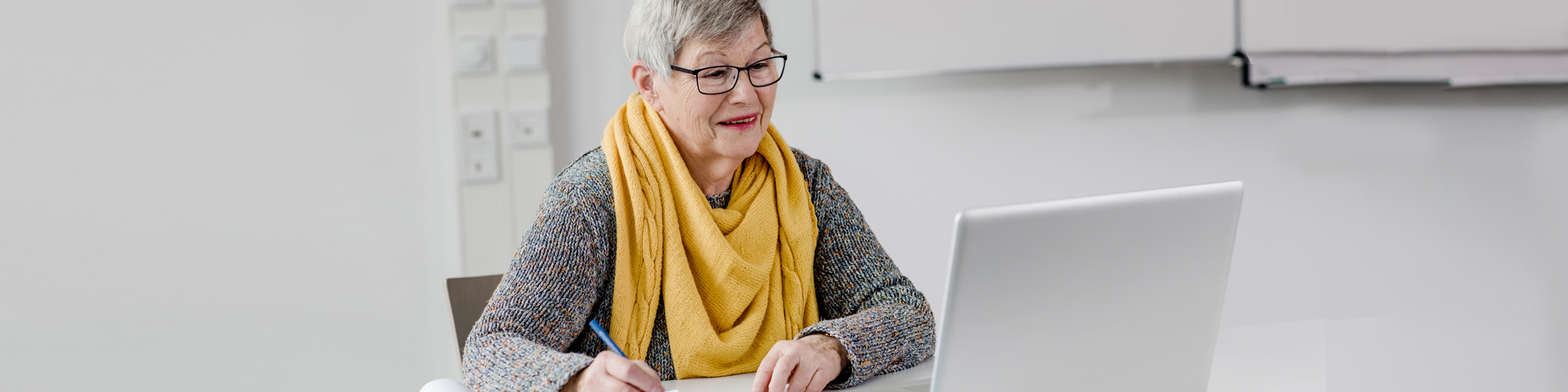 Ältere Frau mit gelbem Schal vor Lap-Top