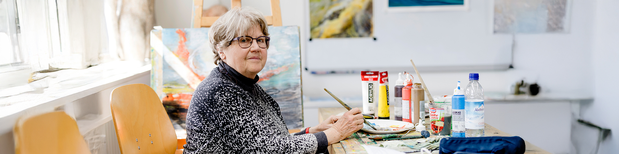 Ältere Teilnehmende eines Malkurses vor einer Staffelei mit Gemälde