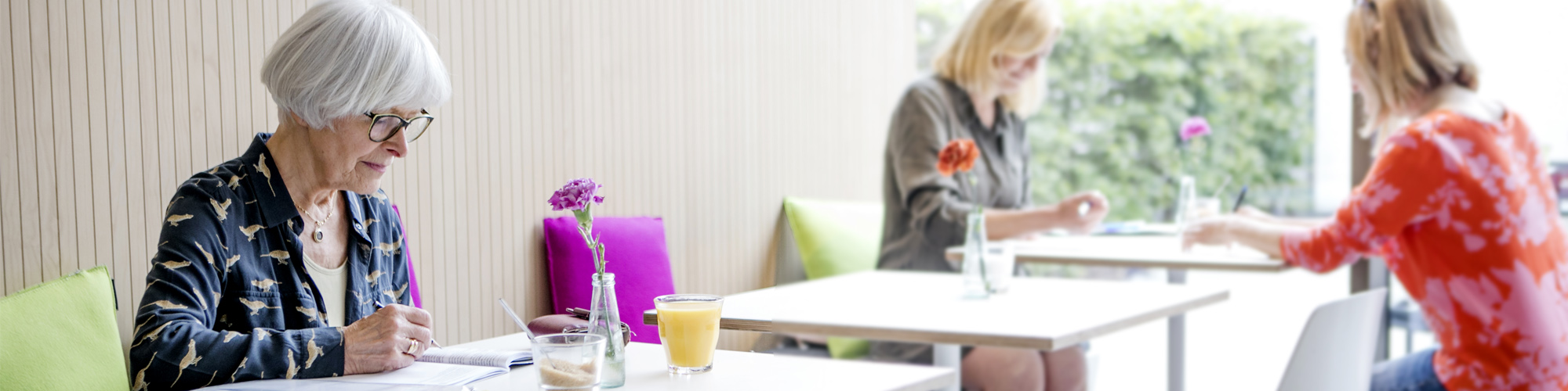 Ältere Dame schreibt konzentriert in ein Übungsheft in einem Café