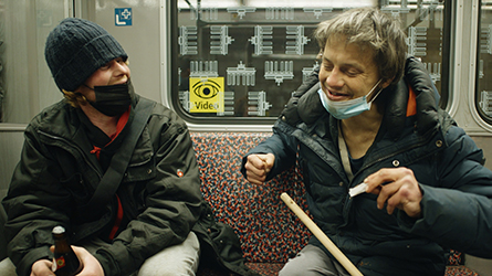 Filmstill aus "Hausnummer Null": zwei sitzende, obdachlose Männer in einer U-Bahn, die sich unterhalten
