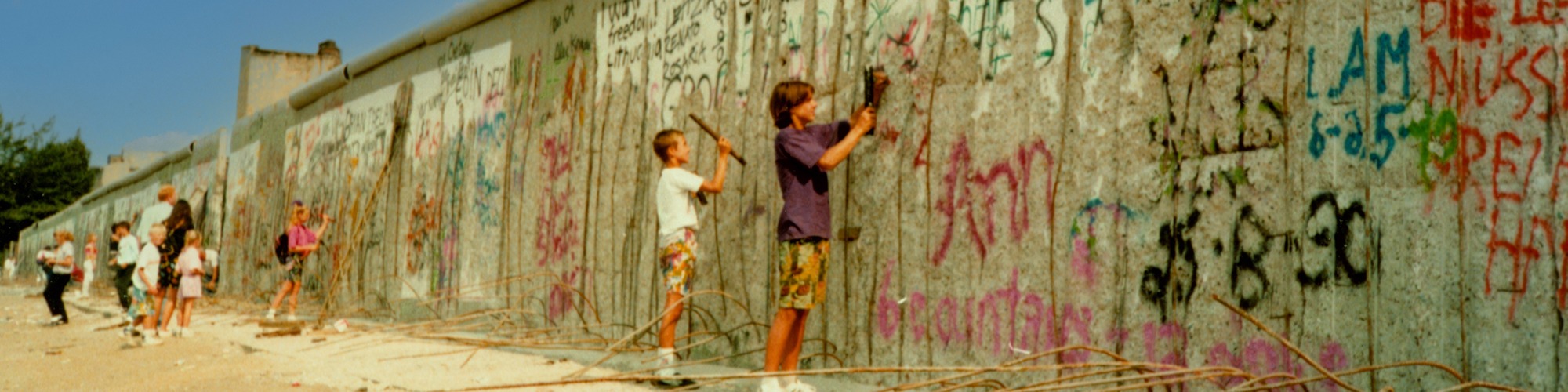 Foto der Berliner Mauer mit Jugendlichen, die Stücke aus der Mauer schlagen